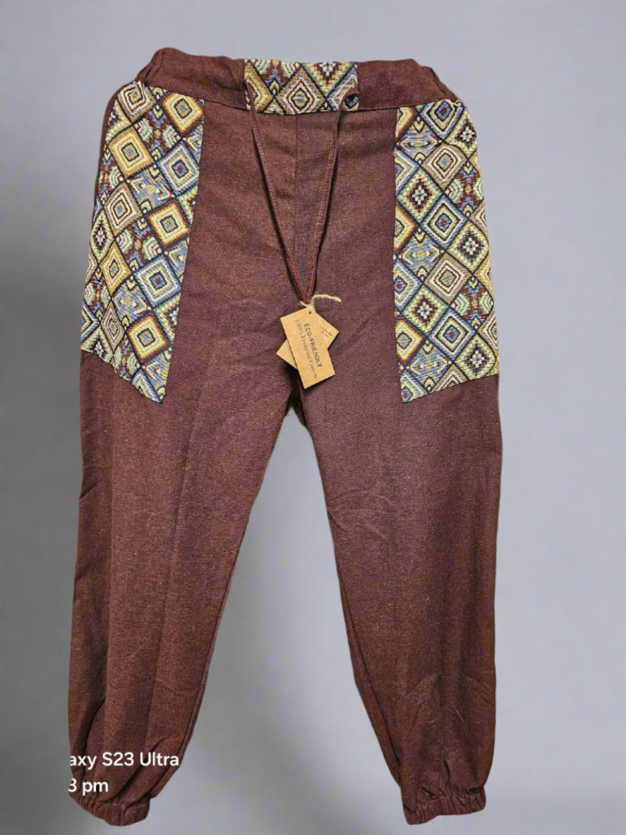 Brown pants with patterned waistband on a hanger against a geometric-patterned wall.