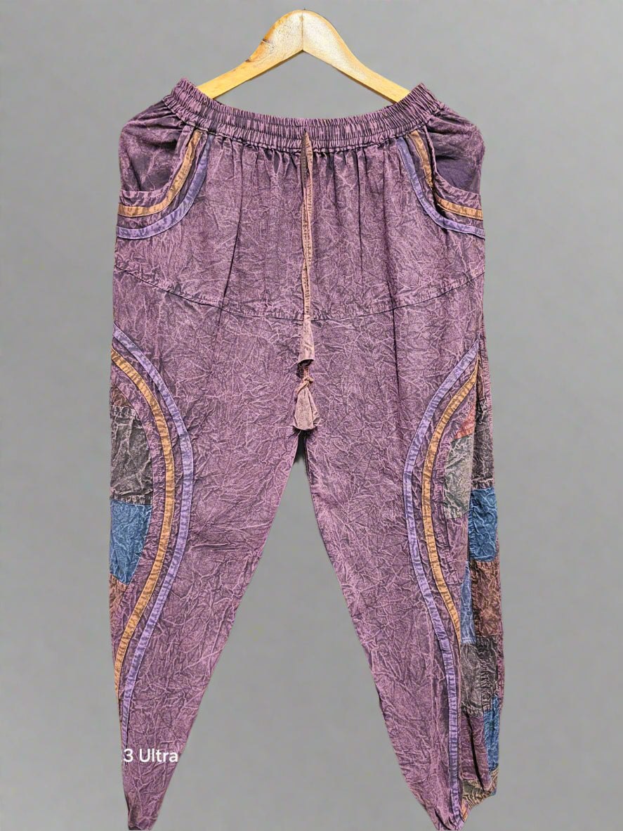 Purple patchwork pants on a hanger against a geometric patterned wall.